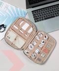 Open view of beige travel electronics organizer case for women with cords, phone, and SD cards beside a laptop, ultra compact size.