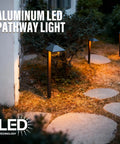 Illuminated yard with 4 Pack 12V Outdoor Landscape Pathway Lighting Kit With 0.6W LED, 3100K Warm White, black aluminum risers at night.