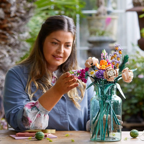 Woman arranging Botanical Flower Bouquet Building Kit With 15 Realistic Stems Like Roses Snapdragons Poppies Asters Daisies And Grasses For Adults in glass vase
