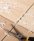 Front view: white cross-shaped tile spacers, 1/16 in, 500 pcs, plastic for tile installation, scattered on wood tiles.