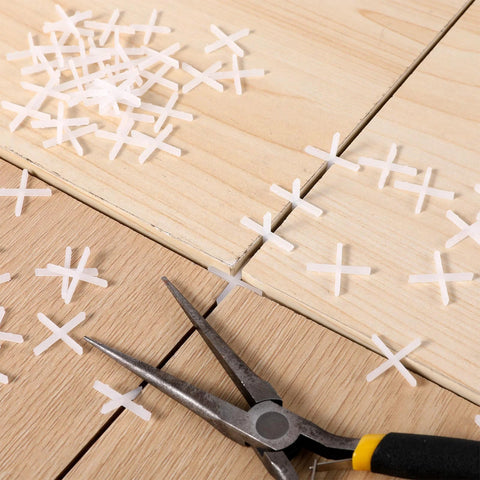 Front view: white cross-shaped tile spacers, 1/16 in, 500 pcs, plastic for tile installation, scattered on wood tiles.