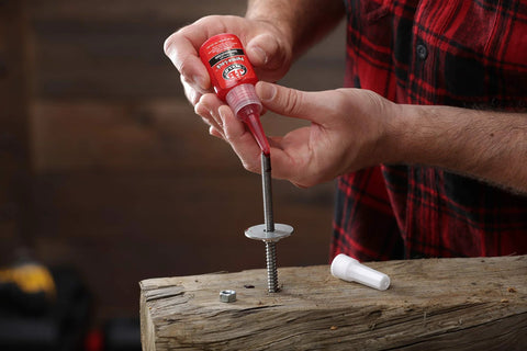 Person applying Red High-Strength Thread Locker That Locks Tight And Seals Like A Boss, 50ml, onto a threaded bolt in a workshop.