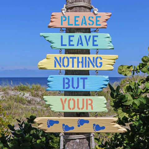 Decorative wooden sign with painted message 'Please Leave Nothing But Your Footprints' against a beach backdrop.