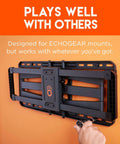 Front view of a black TV wall-mount bracket attached to an orange wall; hand tightening a lag bolt.