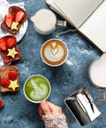 Stainless Steel Milk Frothing Pitcher 6.8oz 200ml With Dripless Spout, next to latte art and breakfast on a blue stone table
