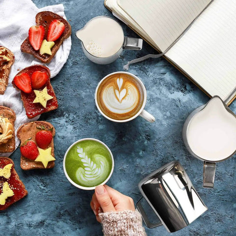 Stainless Steel Milk Frothing Pitcher 6.8oz 200ml With Dripless Spout, next to latte art and breakfast on a blue stone table