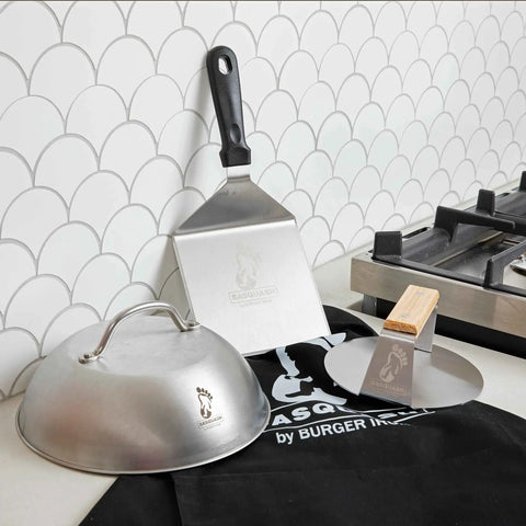 9 Inch Stainless Steel Cheese Melting Dome For Griddles And Flat Tops, Locks In Heat, shown with spatula and grill press on counter