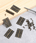 12 Pcs Antique Brass Small Hinges for Jewelry Boxes and Wooden Cabinets with Screws on table with wooden block and screwdriver