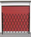 Built Like A Tank Foldable Security Gate 48 By 71 Inch Expandable Iron Frame Barrier mounted against a red garage door.