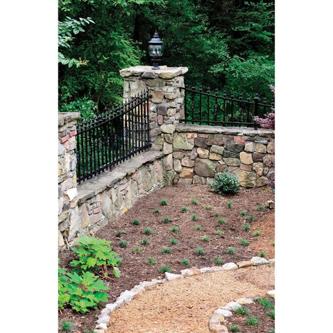 Stone wall and garden path with black iron fence and lamp post in greenery