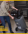 Man moving 29 Gallon Portable Air Compressor With 2.5 HP Motor, 120 Volt Power, 175 PSI Max with flat-free tires in garage