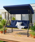 Three Seat Outdoor Porch Swing Glider With Adjustable Canopy Convertible Patio Bed Upgraded Folding Cup Holders Thick Cushions Cozy Up In The Backyard Garden Poolside Blue on a wooden deck.