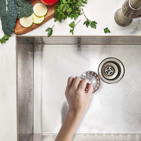 Hand using No Fuss 2 In 1 Kitchen Sink Strainer Stopper with Spring Clip Plunger for Standard 3-1/2 Inch Drains in stainless sink.