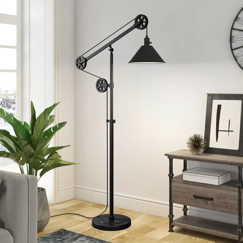 Tall Pulley System Floor Lamp With Metal Shade In Blackened Bronze Finish Adjustable Arc Lighting For Home Office Living Room Or Bedroom Mid Century Modern Style With Dope Industrial Vibe next to a plant and a desk in a bright room.