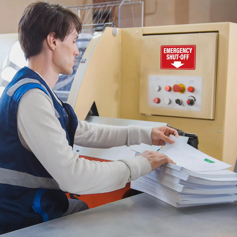 Badass Emergency Shut Off Sign Sticker With Knockout Down Arrow Hella Waterproof Self Adhesive Heavy Duty Safety Marker For Power Tools And Factory Equipment on machine with worker.