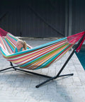 Double Cotton Hammock With Space Saving Steel Stand And Upgraded Polyester End Strings 450 Lb Capacity Premium Carry Bag Included Made From USA Grown Cotton Spacious 63 By 94 Inch Bed For Two Easy Setup And Portable Salsa Color by a poolside
