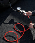 Person using a gauge on a 3/8 Inch By 100 Ft Heavy Duty Hybrid Air Compressor Hose for tire inflation.