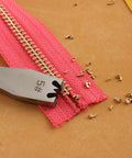 Close-up of Pro Grade Zipper Teeth Remover Tool removing teeth from a zipper on a pink fabric, showing stainless steel construction.