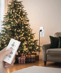 Person using Wireless Remote Outlet Kit For Lights Fans Christmas Lights And Small Appliances, 100ft Range, 10A 1200W near Christmas tree