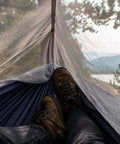 Relaxing inside a Double Tree Hammock With Built In Net For Camping And Travel, view of mountains through mesh netting.