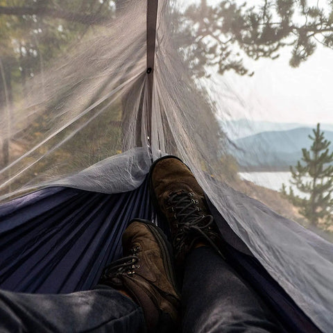 Relaxing inside a Double Tree Hammock With Built In Net For Camping And Travel, view of mountains through mesh netting.