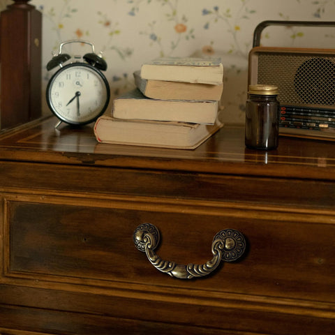 Front view of Six Pack Vintage Drop Bail Cabinet Handles in Antique Brass Finish on a wooden dresser drawer, 3-1/2 inch hole centers.