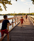 Boy with Scooby Doo Themed Kids Spincast Fishing Combo running on wooden pier toward water, sunny day, trees in background