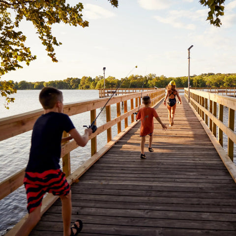 Boy with Scooby Doo Themed Kids Spincast Fishing Combo running on wooden pier toward water, sunny day, trees in background