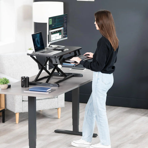 Woman using 32 Inch Desk Converter K Series Sit To Stand Riser With Dual Monitor And Laptop Workspace Height Adjustable