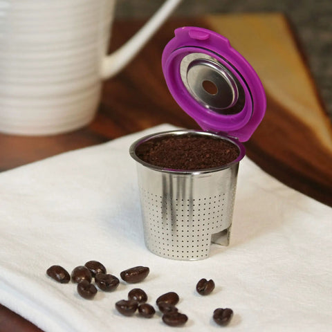 Stainless Steel Reusable K Cup Coffee Pod With Built In Filter For Keurig Single Serve Brewers Eco Friendly And Durable Metal Filter Cup Lets You Brew Fresh At Home Every Morning displayed with lid open, filled with coffee grounds on a cloth.