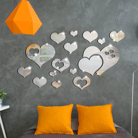 Heart Mirror Wall Decal Set 17 Pieces 3D Acrylic Reflective Stickers Removable Wall Art Decor For Living Room And Bedroom Easy Peel And Stick Waterproof Backed Mirror Art displayed on a grey wall above orange cushions.