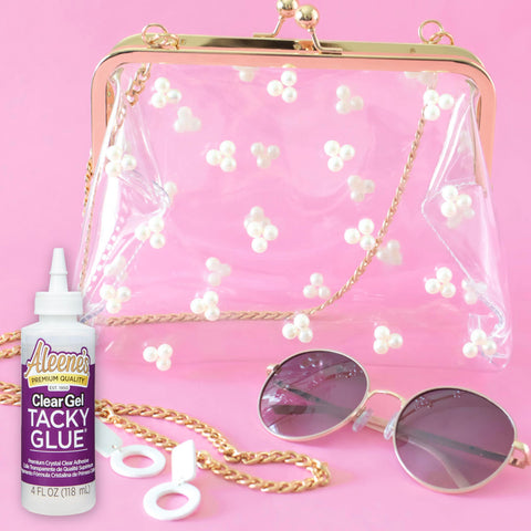 Clear Gel Tacky Glue for Crafts and Slime, 4 oz bottle next to a clear purse with floral decor, sunglasses, and gold chain on pink background