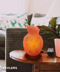 Pineapple-shaped pink Himalayan salt lamp on wooden table beside potted plant and remote in cozy living room.