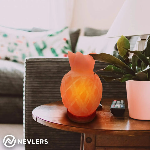 Pineapple-shaped pink Himalayan salt lamp on wooden table beside potted plant and remote in cozy living room.