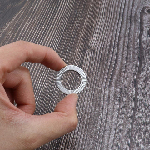 Close-up of a silver manganese steel wedge lock washer held between fingers.