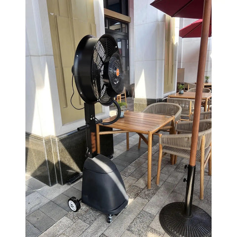 No Sweat Commercial Misting Fan Delivers Beast Mode High Velocity Airflow For Restaurants And Warehouses Featuring Rock Solid Metal Housing And Quick Adjustable Tilt Swivel In Blue set up outdoors beside a wooden table.