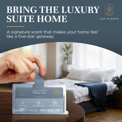 Hand holding white tea scented whole home air freshener system for HVAC filters, bedroom setting in background.