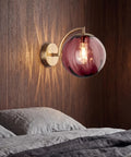 Mid‑Century Modern Globe Glass Wall Sconce with Wine Red Hand‑Blown Glass illuminating a bedroom wall with soft shadows.