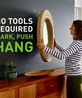 Woman hanging a mirror using Heavy Duty 25 LB Drywall Picture Hangers With Spot Markers No Studs Required Hardened Steel Hooks.