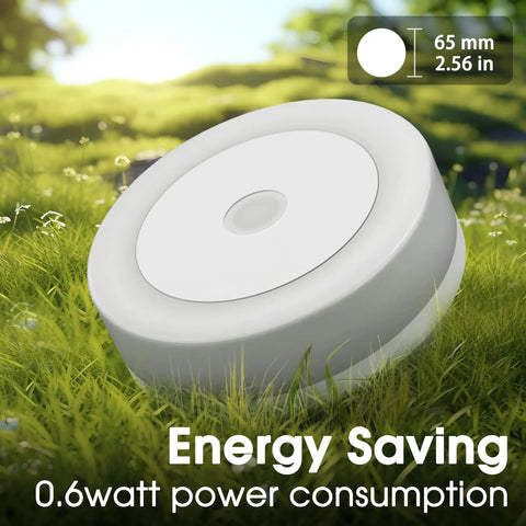 Close-up of white round LED night light with dimensions and energy saving features displayed in grassy outdoor setting.