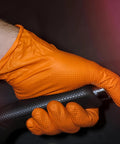 Close-up of orange nitrile glove gripping a textured black handle; heavy-duty, raised diamond grip, XX-Large.