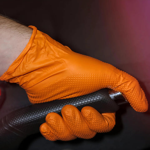 Close-up of orange nitrile glove gripping a textured black handle; heavy-duty, raised diamond grip, XX-Large.
