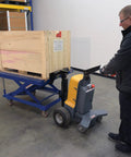Heavy Duty Electric Powered Tugger With 1000 Lb Pull Capacity For Effortless Factory Material Handling featuring ergonomic handle moving a wooden crate.