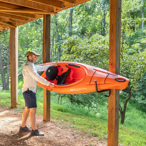 Man using Heavy Duty Swivel Kayak Rack For Garage Walls That Folds Flat Saves Floor Space to store an orange kayak.