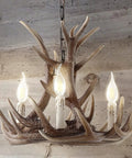 Brown Adjustable Resin Antler Three Light LED Chandelier hanging against a wooden wall, with glowing LED bulbs included.