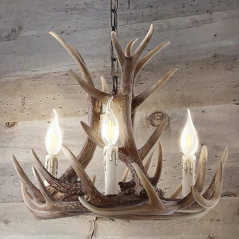 Brown Adjustable Resin Antler Three Light LED Chandelier hanging against a wooden wall, with glowing LED bulbs included.