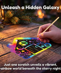 Hand using a stick on Camping Scratch Card Kit 24 Pack For Outdoor Parties with rainbow colors and camp-themed designs.
