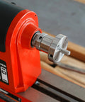 1x8TPI female to 1-1/4x8TPI male thread adapter mounted on red woodturning lathe headstock; silver metal with flange.
