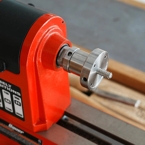 1x8TPI female to 1-1/4x8TPI male thread adapter mounted on red woodturning lathe headstock; silver metal with flange.