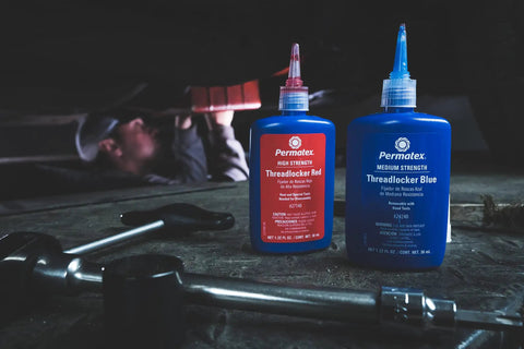 Red High Strength Thread Locker For Heavy Duty From Three Eighths To One Inch Locks Studs And Press Fits Delivers Three Thousand PSI Holding Power To Fight Vibration Loosening And Keep Things Tight For Removable Or Permanent Installations Six Ml Tube bottle next to blue medium strength bottle in workshop